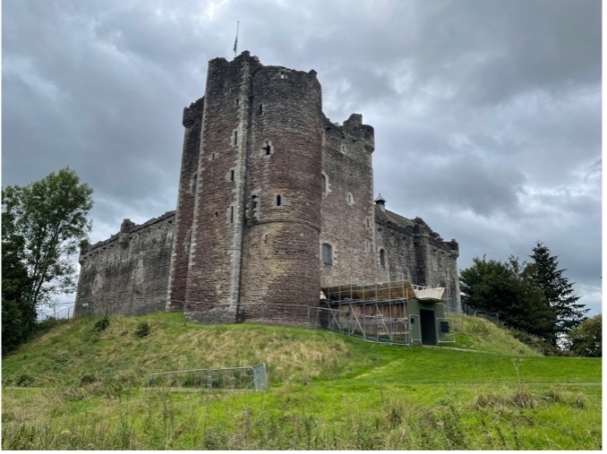 A large, old castle sits on top of a hill of green grass. The sky is dark and stormy.