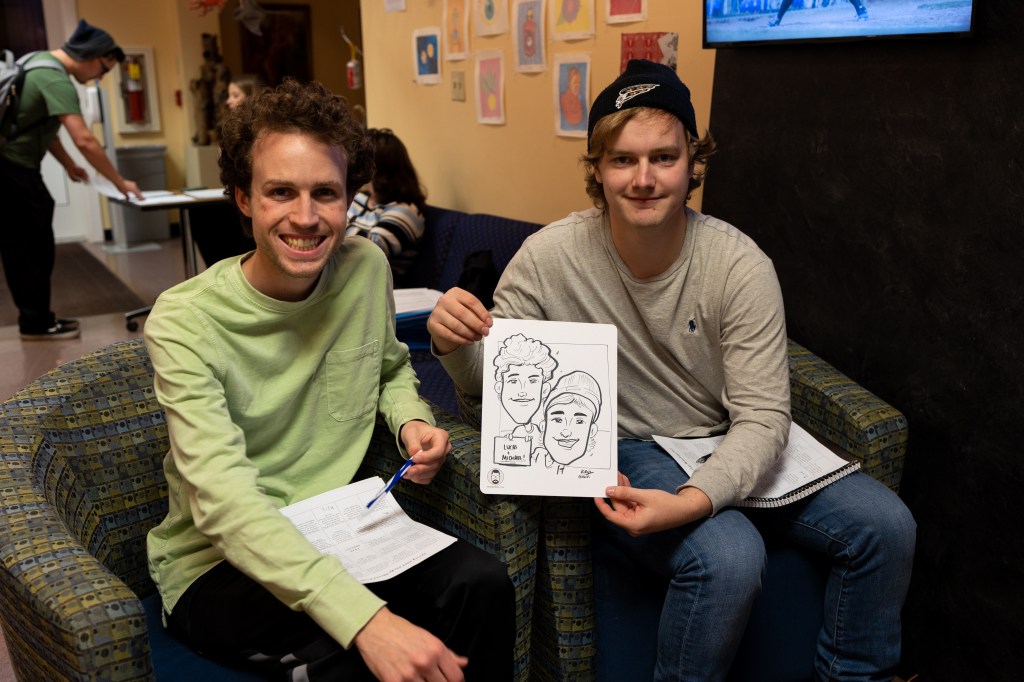 Two boys pose with a drawn caricature of themselves.