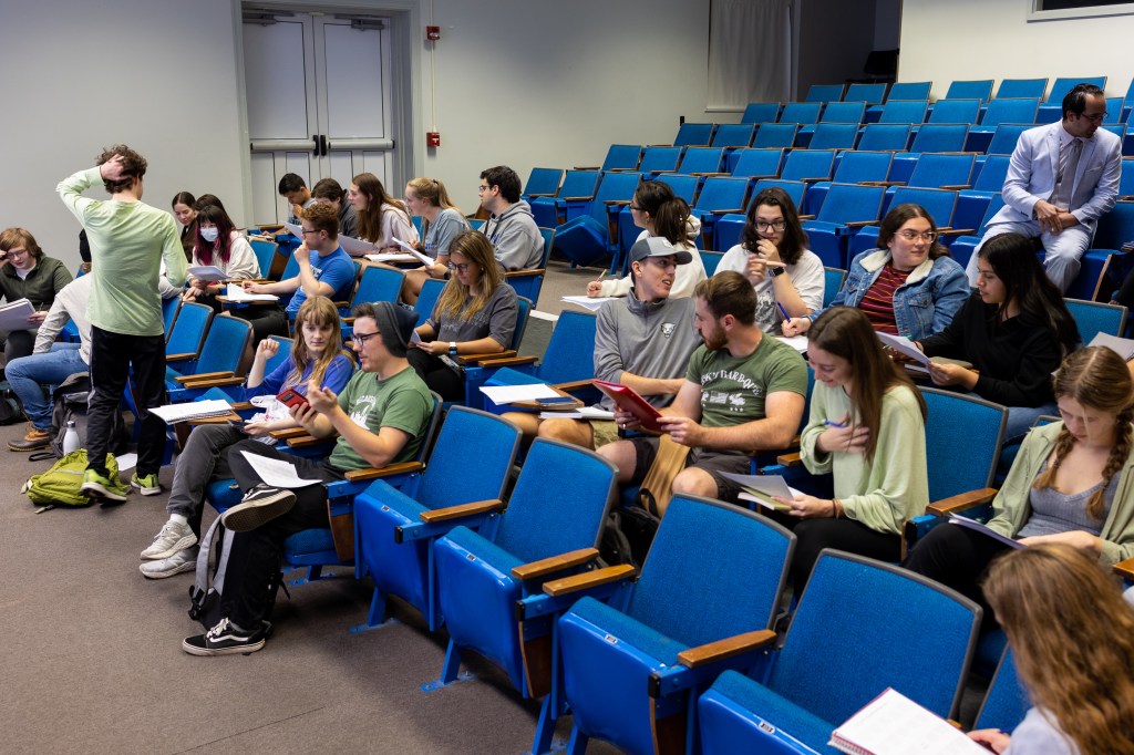 A group of students sit in blue seats in an auditorium.