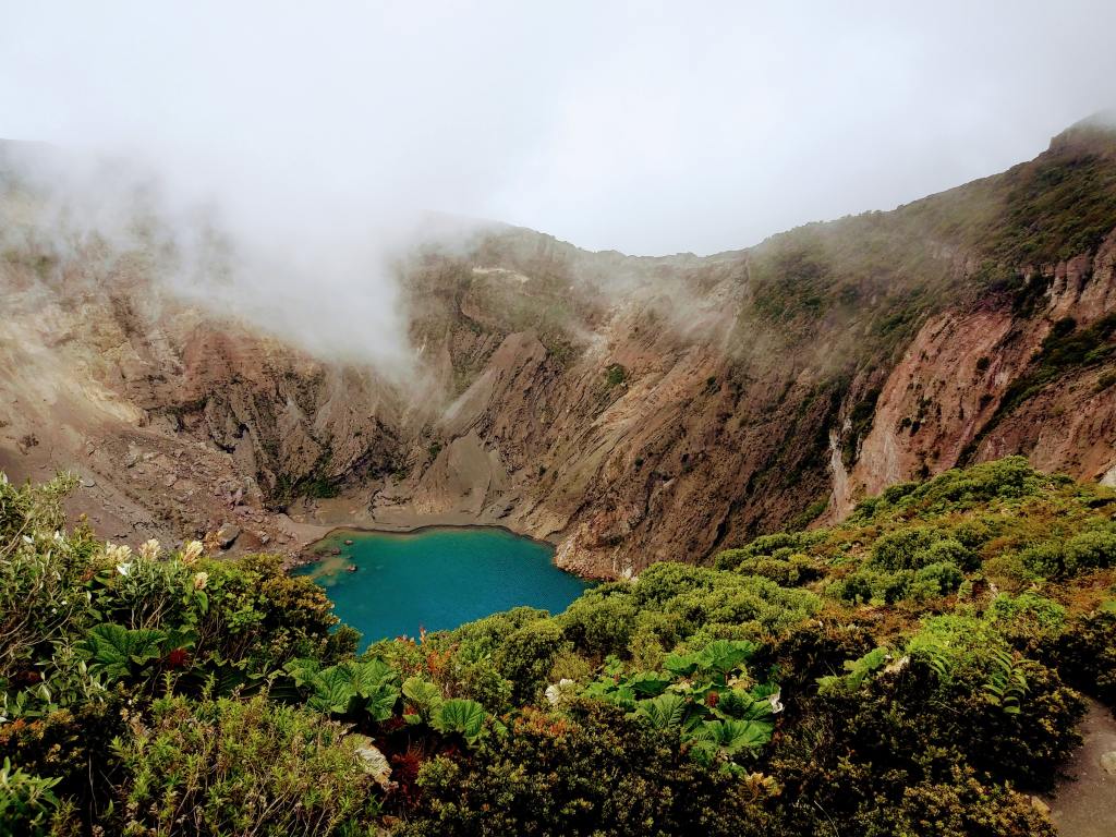 A bright blue pond is surrounded by brown mountains and lush green greenery in Costa Rica.