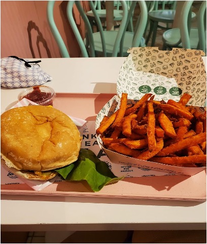 A burger and sweet potato fries sit on a platter on a white table.