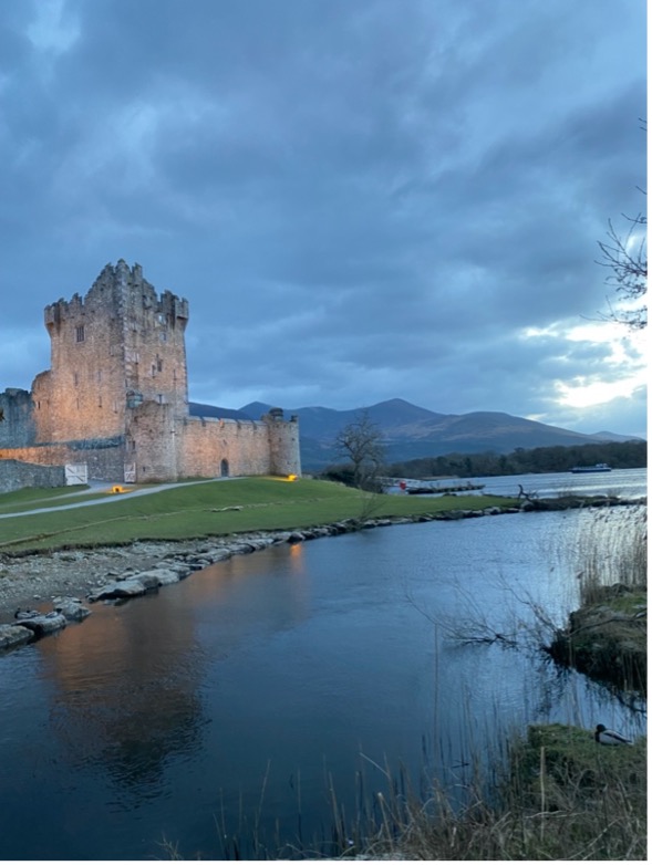 Ross Castle in Killarney National Park sits on a green, grassy hill behind a small river.