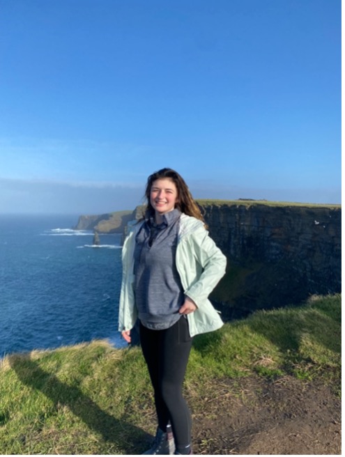A girl stands on the edge of the Cliffs of Moher in Scotland.